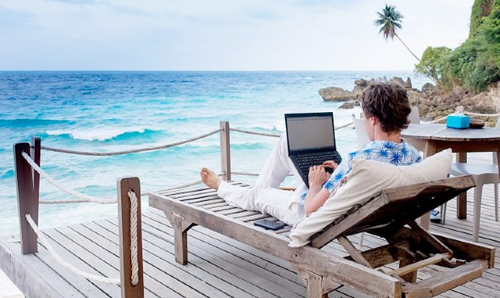 An image representing a person working with laptop on the seaside